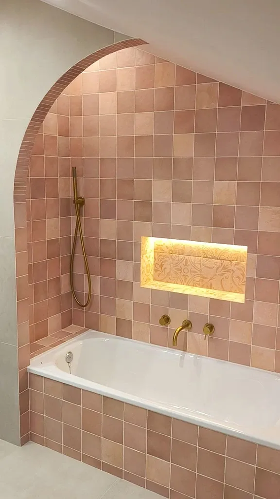 Baño del ático con cerámica rosa artesanal y grifería dorada